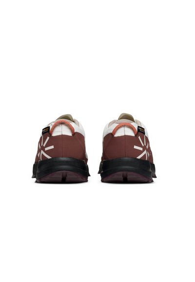 Une paire de chaussures de sport marron et blanche avec des semelles noires vue de l'arrière, présentant des motifs éclatants réfléchissants et des boucles de talon rouges.