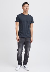 Mørkegrå kortærmet t-shirt med rund hals og venstre brystlomme, parret med slidte sorte jeans og hvide sneakers med sorte striber.