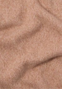 Gebreide stof in zacht roze met een fijne ribbelstructuur, waarin subtiele kleurvariaties en een delicate, warme uitstraling te zien zijn.