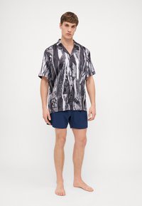 Short-sleeve black and white patterned shirt featuring a collared design, paired with dark blue shorts. The shirt has a loose fit.