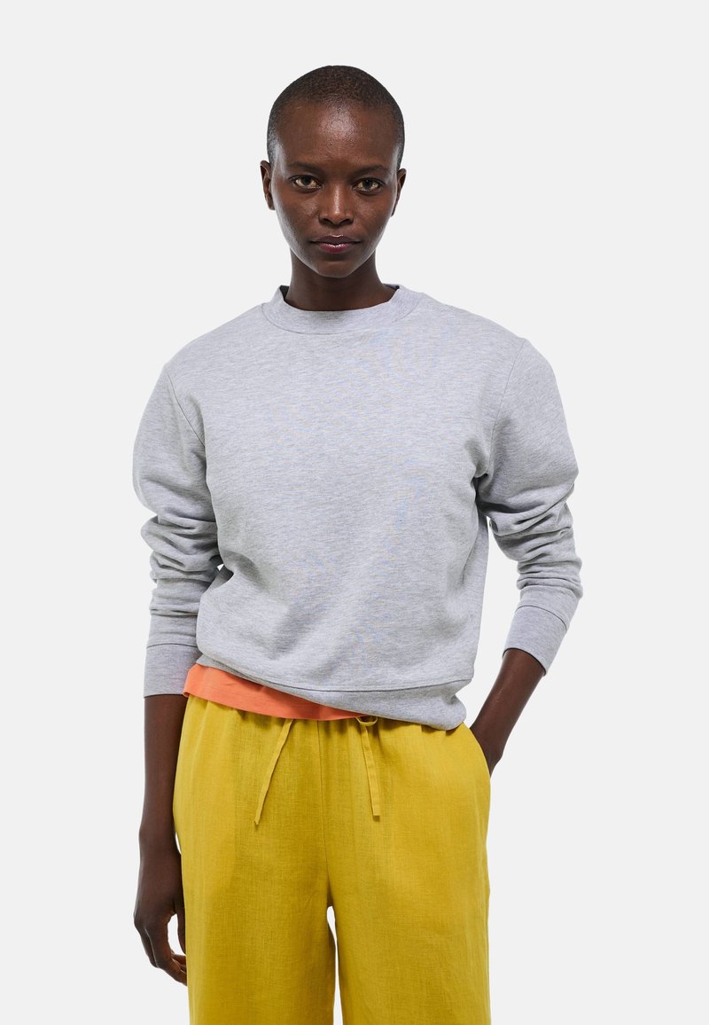 Sweatshirt gris à col rond et poignets côtelés, superposé à une chemise orange. Associé à un pantalon jaune à cordon de serrage. Design simple.