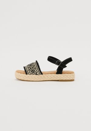 Sandal preto e castanho com tira de tecido trançado apresentando padrões geométricos; sola estilo juta; tira ajustável no tornozelo. Design plano.