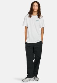 Witte t-shirt met korte mouwen met "ELEMENT" in het groen gedrukt. Een paar zwarte loszittende broek en grijze sportschoenen met zwarte accenten.