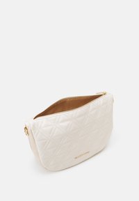 Beige prošívaná kožená taška se zipovým uzavřením, hladkým povrchem a zlatými kovovými doplňky. Na přední straně je vystouplé logo.