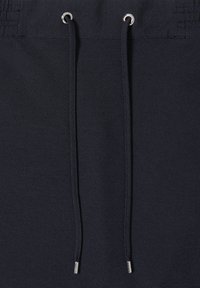 Dunkelblauer Stoff mit strukturierter Webart, versehen mit Metallösen und schwarzen Kordelzügen mit silberfarbenen Enden am Bund.