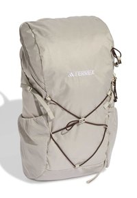 Zaino beige con superficie testurizzata, tasche laterali in rete e spallacci regolabili. Presenta un sistema bungee frontale e un logo bianco.