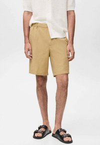 Beiga shorts i bomull med skräddarsydd passform, med sidofickor och dragkedja. Matchas med en vit, stickad skjorta med knappar och svarta sandaler.