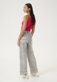 Top fucsia senza maniche abbinato a jeans in denim grigi chiari a gamba larga con due tasche posteriori e orli arrotolati, su uno sfondo neutro.