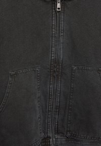 Jachetă neagră cu fermoar, evidențiată printr-un fermoar solid, material texturat, două buzunare frontale și cusături vizibile pe margini.