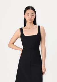 Rochie neagră fără mâneci, cu decolteu pătrat, corset ajustat și fustă fluidă. Materialul are o textură netedă, cu detalii minime.
