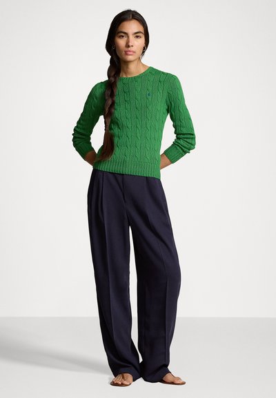 Grønn kabelstrikket genser med rund hals, sammen med løstsittende navy bukser, med en glatt tekstur og avslappet design.