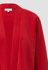 Czerwony kardigan w stylu kimono, otwarty z przodu, o gładkiej teksturze i zwiewnym fasonie. Wykonany z lekkiej tkaniny, z delikatnym układem fałd.