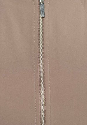 Close-up van een zilveren rits die half dicht is op glad beige stof met zichtbare stiksels langs de ritsranden.