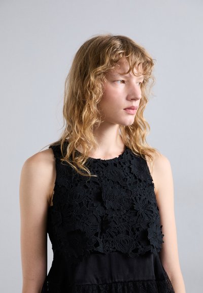 Mustmustrits mustrikk lillede pitsiga, millel on tekstuuriga tõstetud detailid. Eemaldatavad varrukad, pehme kangas ja kihiline disain.