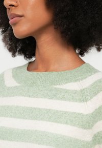 Heleroheline ja valge triibuline kampsun soonikkoes kaelusega. Pehme tekstuur, lõdvestunud istuvus ja kergelt langenud õmblustega õlad.