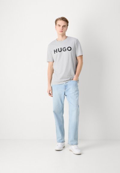Сив котонен потник с "HUGO" в дебели черни букви, съчетан със светло синьо право дънки и бели маратонки. Проста визия, удобен фит.