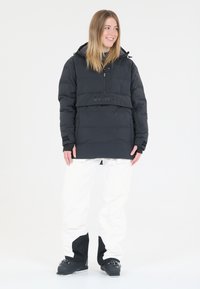 Svart puffjacka med hög krage och framdraget blixtlås, med ett horisontellt band med texten "SLOPE". Kombinerat med vita snöbyxor och svarta stövlar.