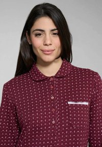 Camicia color borgogna con colletto, motivo a spirale bianco, sette bottoni e tasca con rifinitura bianca. Tessuto morbido con una texture liscia.