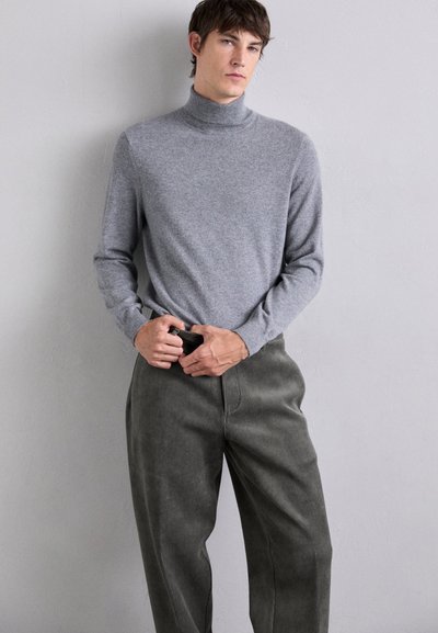 Maglione a collo alto grigio chiaro in tessuto morbido, abbinato a pantaloni in velluto a coste verde scuro, caratterizzati da una vestibilità comoda e sottili righe verticali.