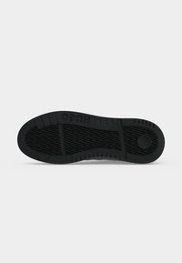 Semelle d’une chaussure noire avec motif d’adhérence texturé, lignes horizontales de la bande de roulement, détail circulaire près du talon et « HUGO » embossé près de la voûte plantaire.