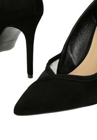 Czarne zamszowe buty na wysokim obcasie z ostrym noskiem, z siateczkowymi wycięciami i błyszczącym, gładkim wnętrzem. Projekt na obcasie typu szpilka.