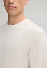 Helle beige, strukturierte Strickpullover mit Rundhalsausschnitt. Verfügt über gerippte Bündchen und Saum, taillierte Form und eine glatte, weiche Oberfläche.