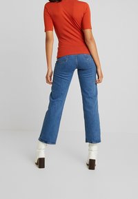 Czerwona bluzka z krótkim rękawem zestawiona z niebieskimi dżinsami w stylu dzwonów. Białe, wysokie na kolano, obcasy. Stylizacja charakteryzuje się gładką fakturą i swobodnym krojem.