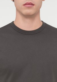 Μπλουζάκι από βαμβάκι σε σκούρο γκρι με λείος υφή. Διαθέτει κλασικό στρογγυλό λαιμόκοψη και κοντά μανίκια. Χωρίς εμφανή διακοσμητικά ή σχέδια.