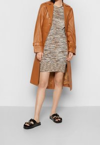 Brun läder trench coat, mönstrad klänning med figursydd passform i beige och bruna nyanser, svarta sandaler med guldkedjedetalj.