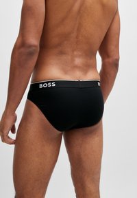 Schwarze Baumwollslips mit tailliertem Design, ausgestattet mit einem BOSS-Logo auf dem elastischen Bund, glatter Textur und ohne sichtbare Muster.