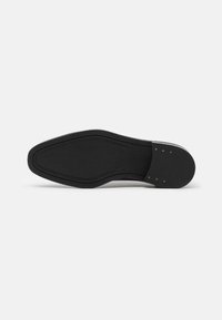 Semelle de chaussure en cuir noir avec une texture lisse, une forme allongée et un profil de semelle à motif pour l'adhérence. Présente de petits accents matériels circulaires.