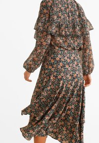 Robe florale en tissu transparent ; fond sombre avec des fleurs roses et orange. Présente des manches volantes et une jupe fluide avec du mouvement.