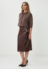 Braune Bluse mit Kragen-Design, kombiniert mit einem knielangen braunen Paillettenrock. Schwarze spitze Absatzschuhe runden das Outfit ab.