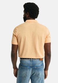 Kortermet polo skjorte i lys oransje, laget av bomull. Har en klassisk krage og en avslappet passform, paret med blå denim jeans.