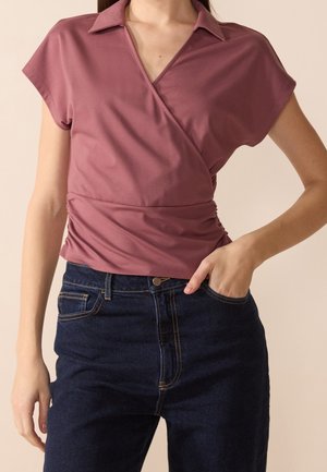 Wikkelstijl top van mauve stof met korte mouwen en een kraag, gecombineerd met donkerblauwe high-waisted jeans met lichte stiksel details.