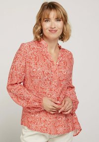 Blouse rouge à motif paisley avec un col montant, une patte de boutonnage et des manches froncées. Tissu lisse avec un léger éclat.