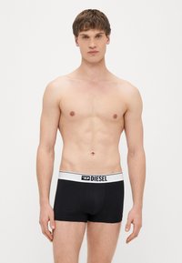 Melnas bokseršorti ar baltu jostu, kurā ir uzraksts "DIESEL" treknā drukā. Gluda auduma un pieguļošs piegriezums bez rakstiem.