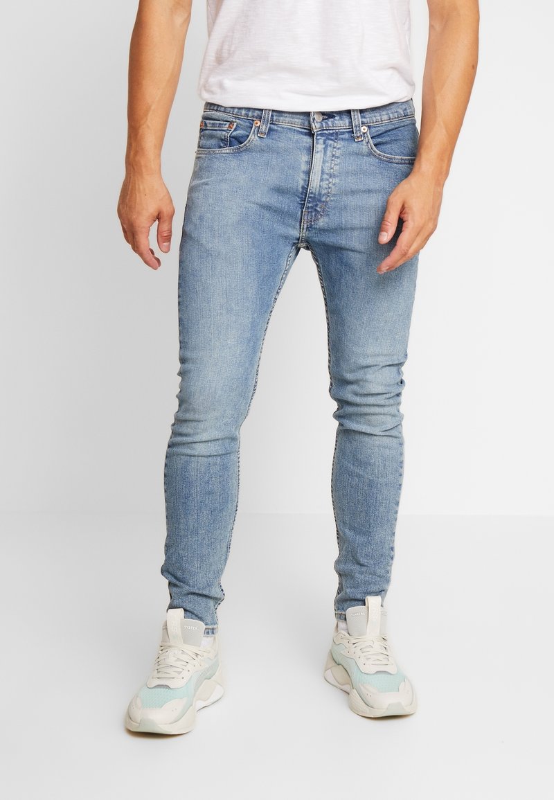 Lichtblauwe slim-fit jeans van denim, met een vijf-pocket ontwerp en subtiele vervaging, gecombineerd met witte en mintgroene sneakers.