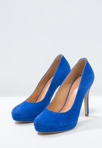 Modré semišové vysoké podpatky s oválnou špičkou, s hladkým vnitřním podšívkou a platformovým designem, umístěné na štíhlém jehlovém podpatku.
