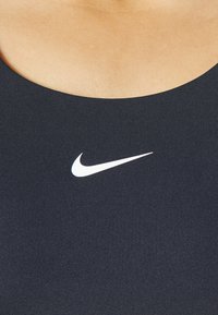 Costume sportivo nero con texture a coste, caratterizzato da un logo Nike swoosh bianco al centro. Scollatura rotonda.