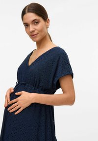 Abito premaman blu navy con maniche corte, scollatura a V e motivo ad occhio di pernice. La vita regolabile mette in risalto la silhouette. Tessuto morbido e traspirante.