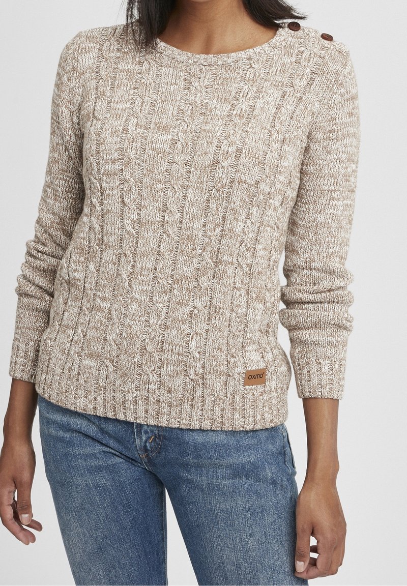 Beige kabelgebreide trui met een ronde halslijn, lange mouwen en knoopdetails op de schouder; heeft een klein merklabel aan de zoom.