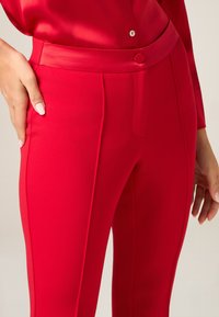 Rode nauwsluitende broek met een gladde textuur, zijzakken, een knoopsluiting en verticale naaddetails voor extra structuur.