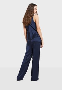 Navy satynowy komplet z koszulą na ramiączkach i spodniami o szerokich nogawkach, charakteryzujący się luźnym krojem, gładką fakturą oraz minimalistycznym wzornictwem bez widocznych wzorów.