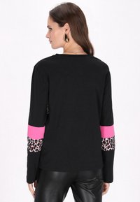 Schwarzes Longsleeve-Oberteil mit rosa Bündchen, das Akzente im Leopardenmuster an den Ärmeln aufweist. Glatter Stoff mit lockerer Passform und rundem Ausschnitt.