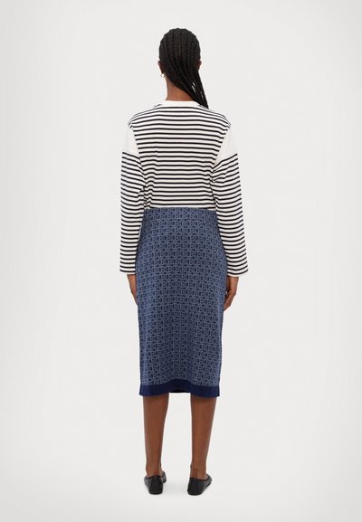 Stripet langermet topp med et marineblått mønstret skjørt, som har rette linjer og kne-lengde design. Sorte leiligheter fullfører antrekket.