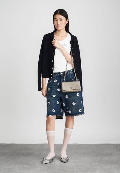 Cárdigan de canalé oscuro sobre una camiseta blanca, combinado con pantalones cortos de mezclilla con adornos florales. Medias ligeras y transparentes y zapatos plateados.