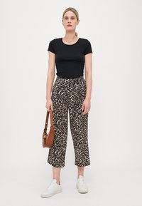 Schwarzes, eng anliegendes T-Shirt, weite Hosen mit Leopardenmuster, weiße Turnschuhe und eine braune Umhängetasche. Strukturiertes Material mit elastischem Bund.