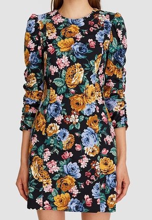 Robe noire à manches bouffantes ornée d'un motif floral vif en jaune, bleu, rose et vert, portée par une personne debout.