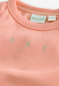 Persikofärgad ribbad T-shirt med rund hals och tryckt "BAKER" i ljusgrön text. Har en subtil textur och mjukt material.